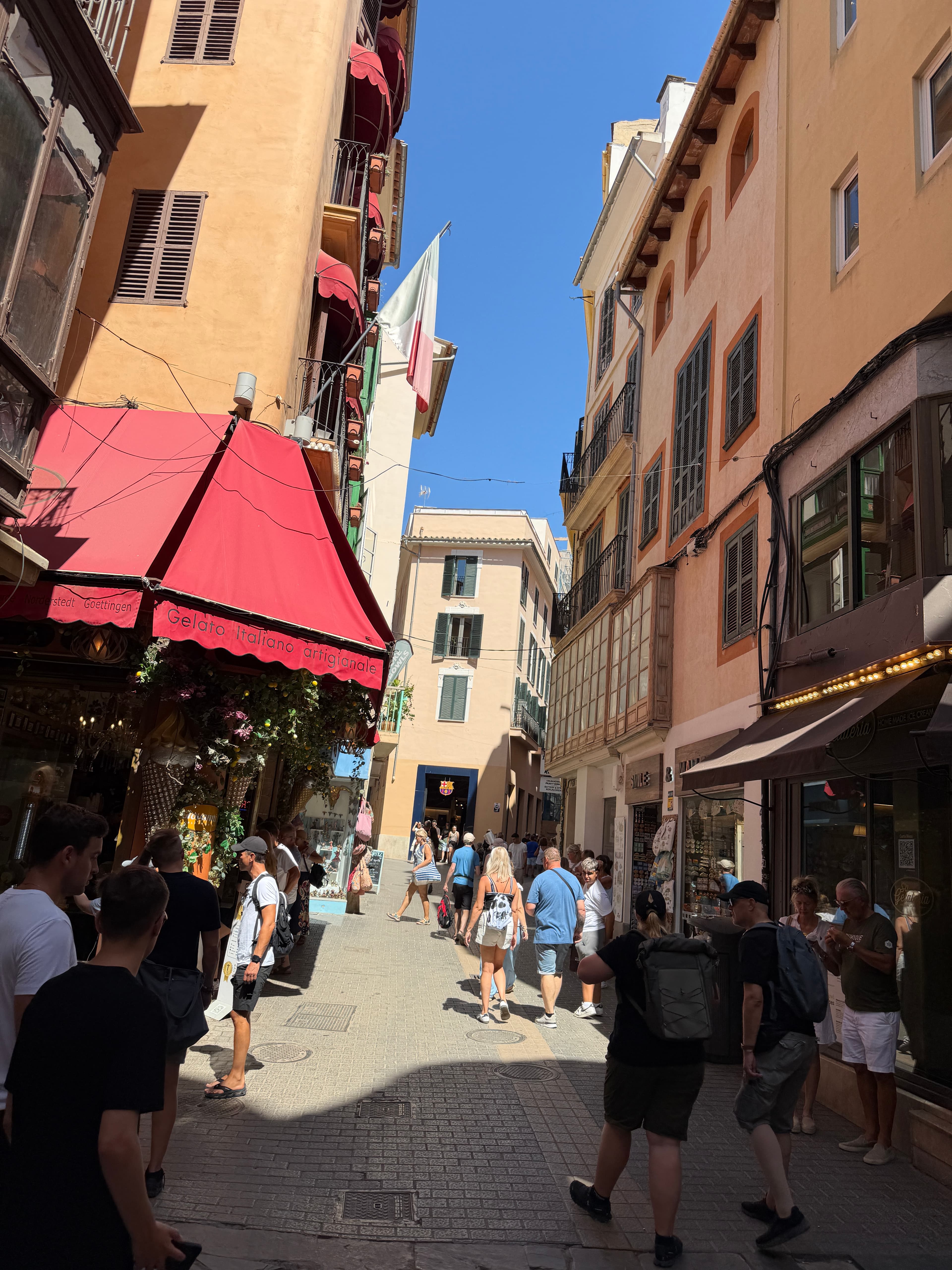 Belebte Einkaufsstraße mit bunten Fassaden und roter Gelateria-Markise in Palma