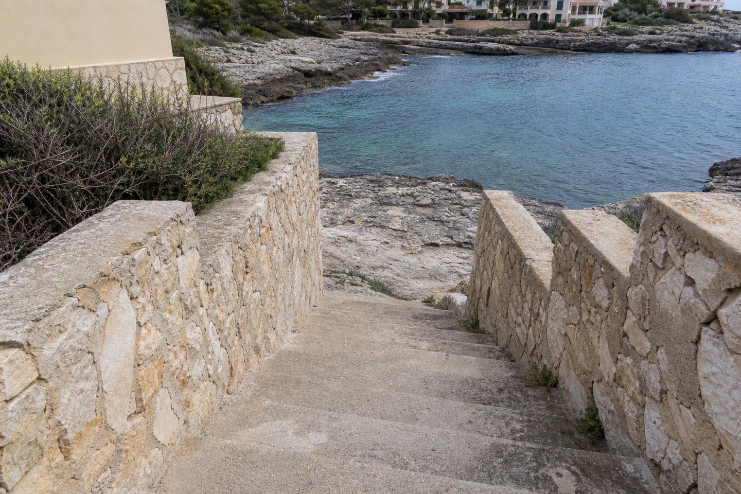 KI-generiertes Stimmungsbild eines plausiblen schlichten Treppenzugangs an der felsigen Küste von Cala Morlanda