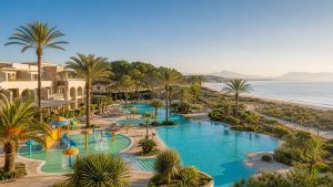 KI-generiertes Stimmungsbild einer familienfreundlichen Poollandschaft direkt am Sandstrand von Playa de Muro – keine Originalaufnahme des Grupotel Alcudia Pins.