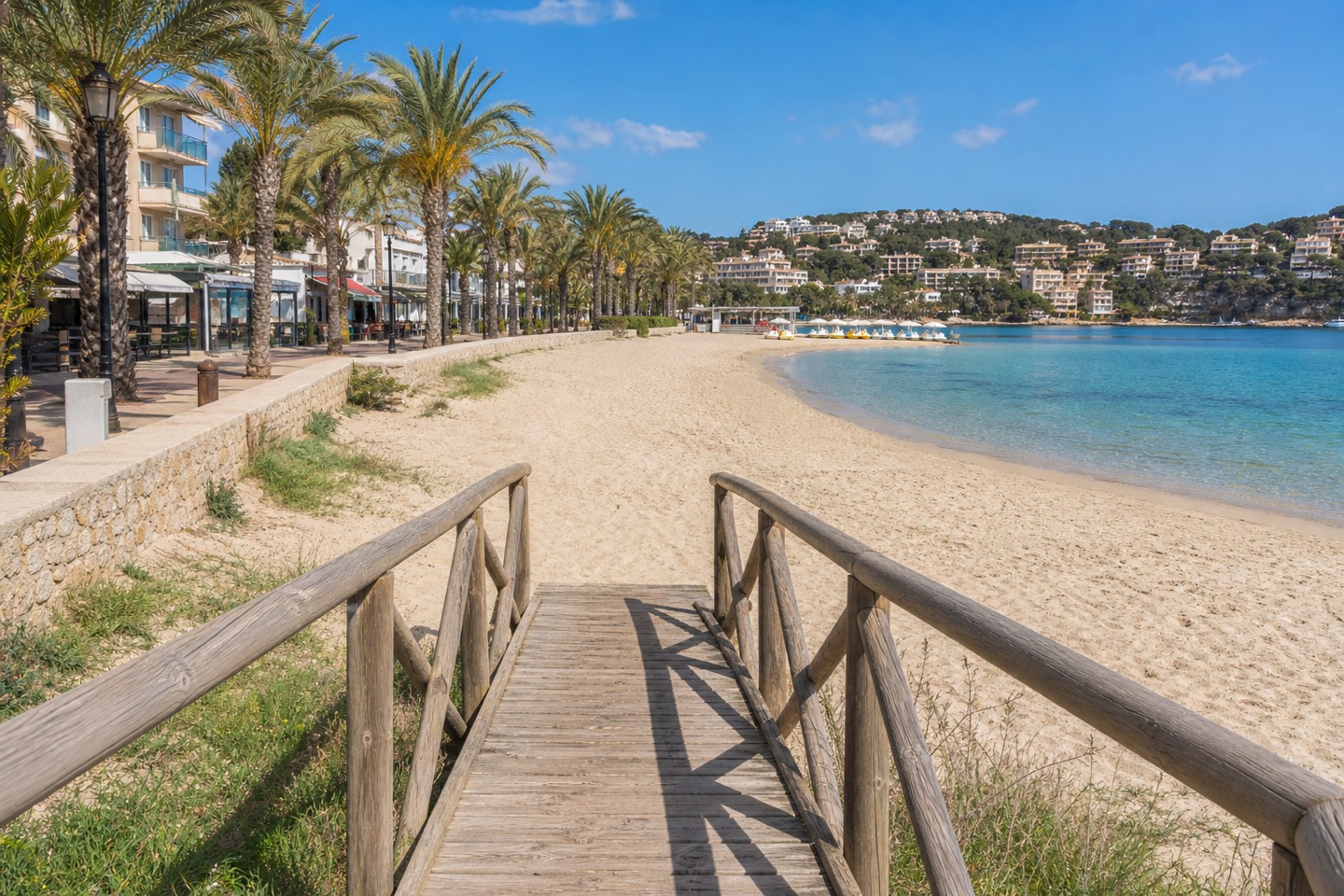 KI-generiertes Stimmungsbild eines Holzstegs zur Platja Palmira mit Palmenpromenade, feinem Sand und ruhiger Bucht